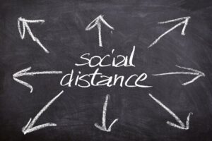 A black background with "social distance" written in white chalk with eight arrows pointing different directions