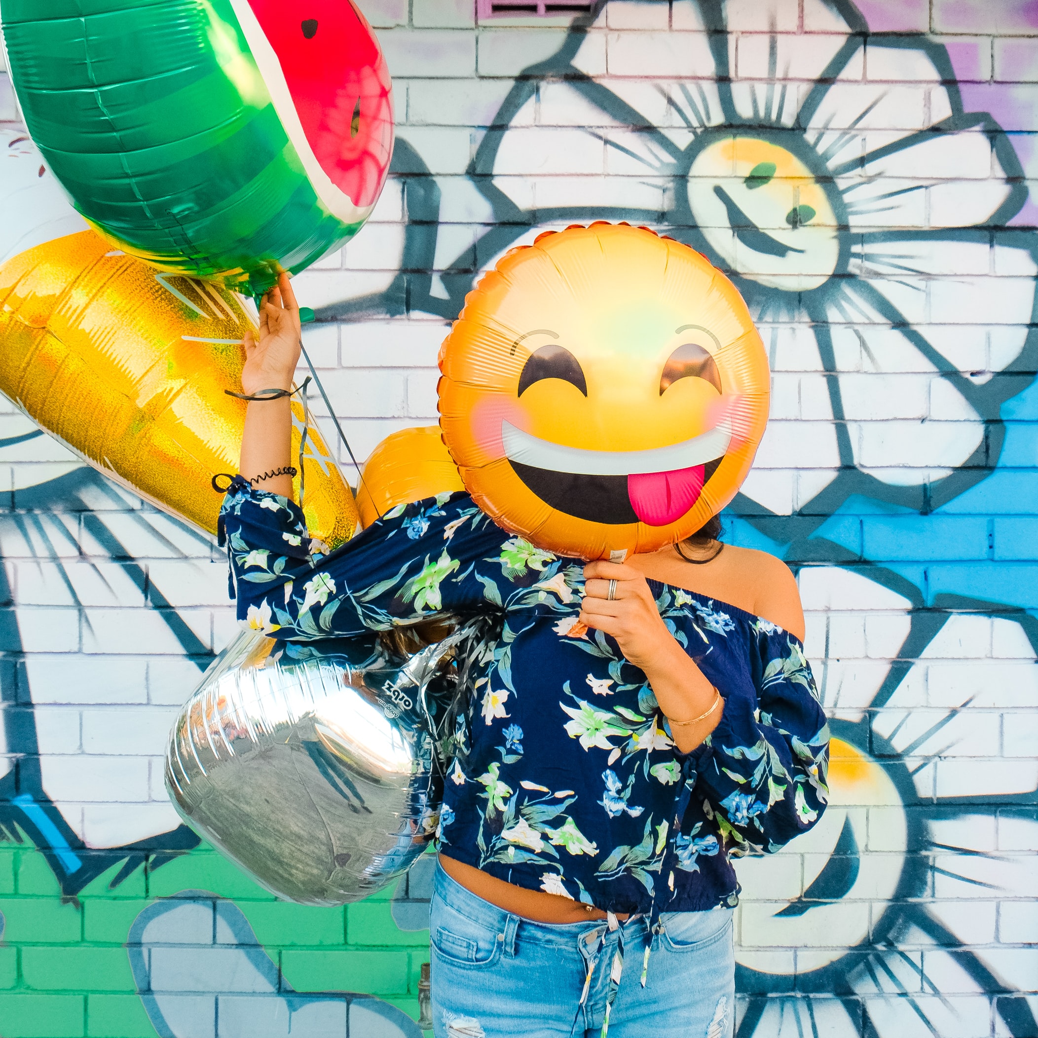 Girl in front of colorful wall holding emoticon balloons