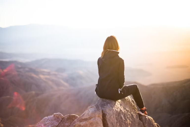 Girl sitting on the edge of a cliff overlooking a vast landscape