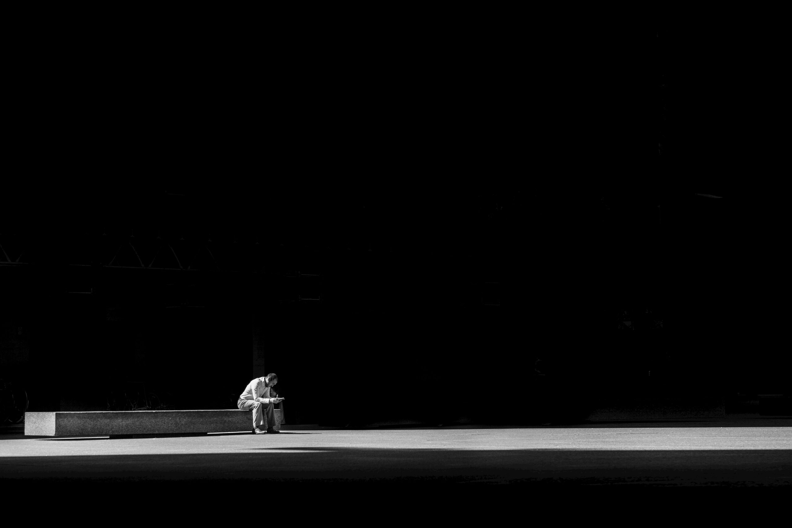 Simple black and white picture of a man sitting alone on a bench used to convey a feeling of loneliness.