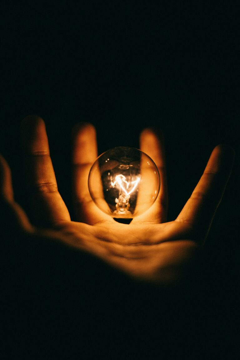 A hand holding a warm but dimly lit light bulb